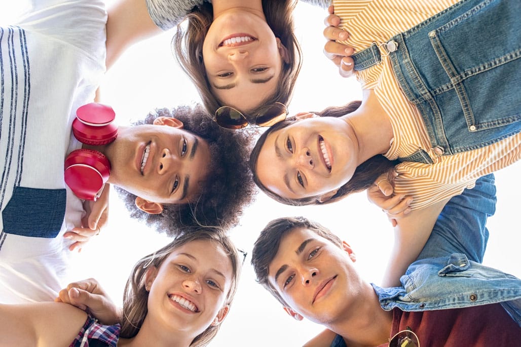 Five smiling friends stand close together in a circle, looking down at the camera, showcasing true group collaboration representing "Tuning in to Kids and Teens at Crossroad Counselling Practice Five smiling friends stand close together in a circle, looking down at the camera, showcasing true group collaboration representing "Tuning in to Kids and Teens at Crossroad Counselling Practice